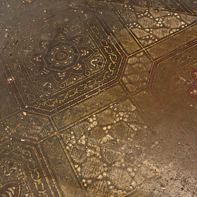 Linoleum or oil cloth flooring from sometime before 1917 with a golden and red pattern of geometric flowers at the center of ornate squares. 