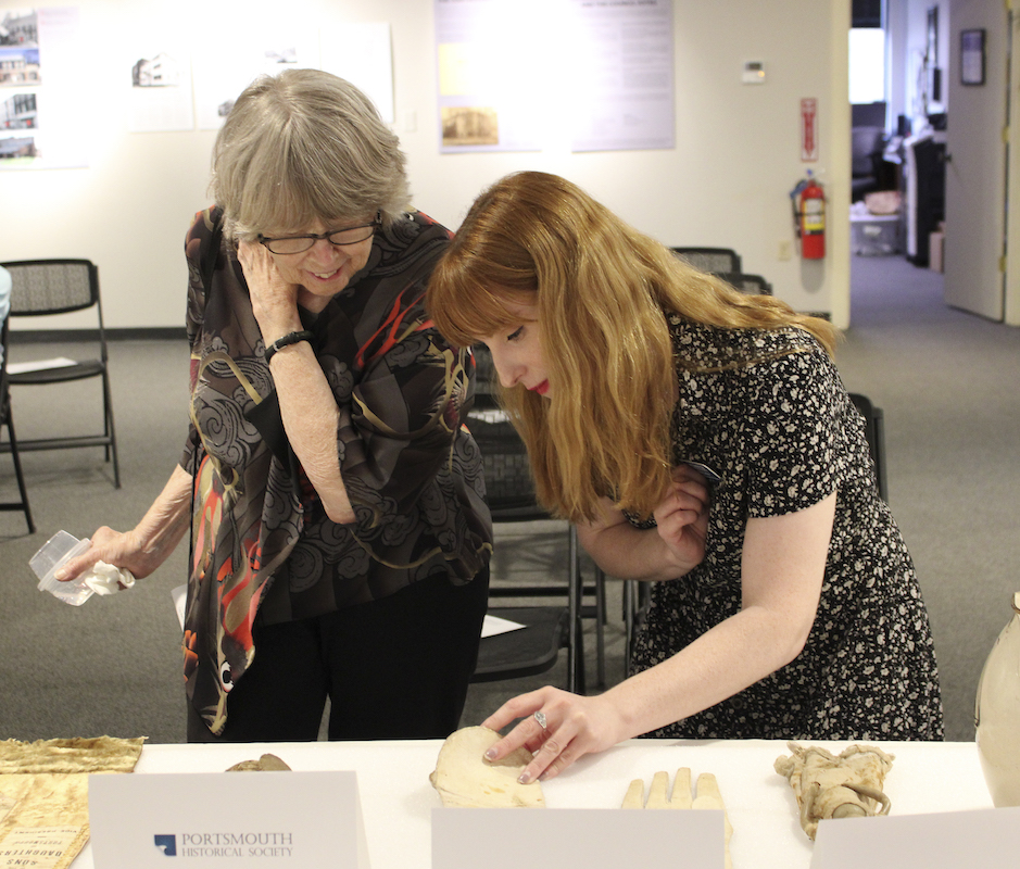 Two individuals looking at the detail on a pair of 19th century funerary gloves.