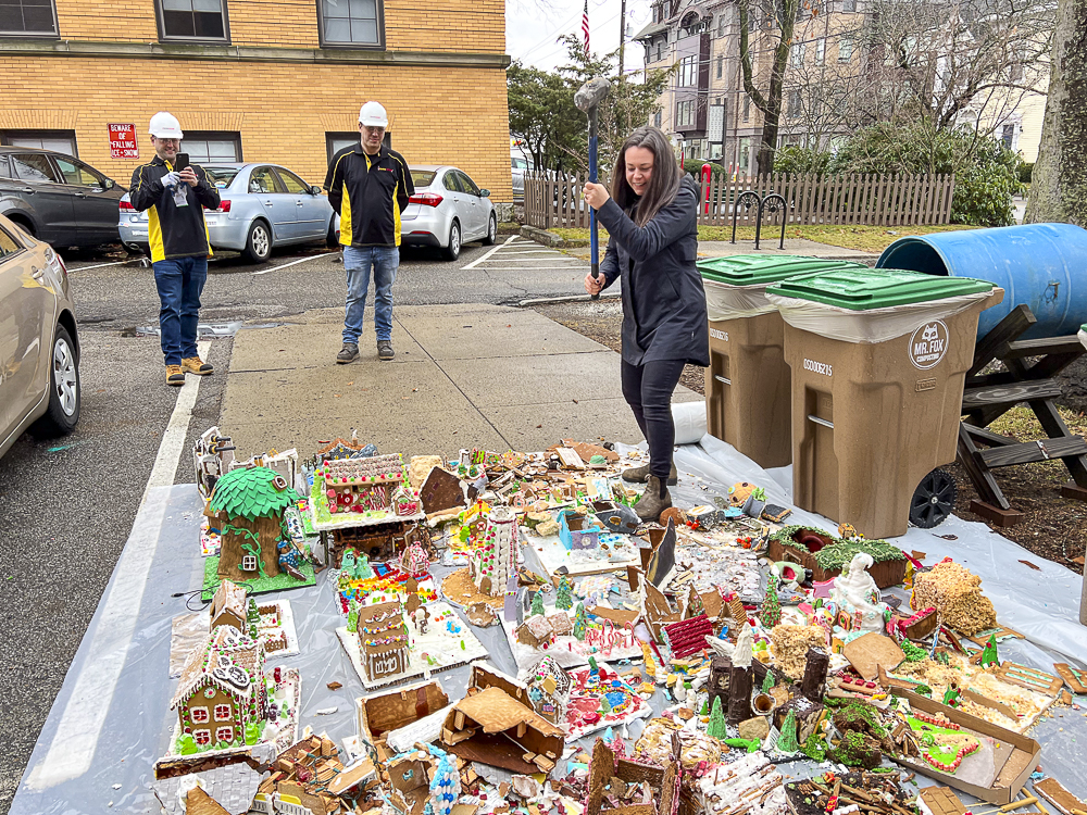 Person with a sledge hammer stands over two dozen gingerbread houses for demolition.